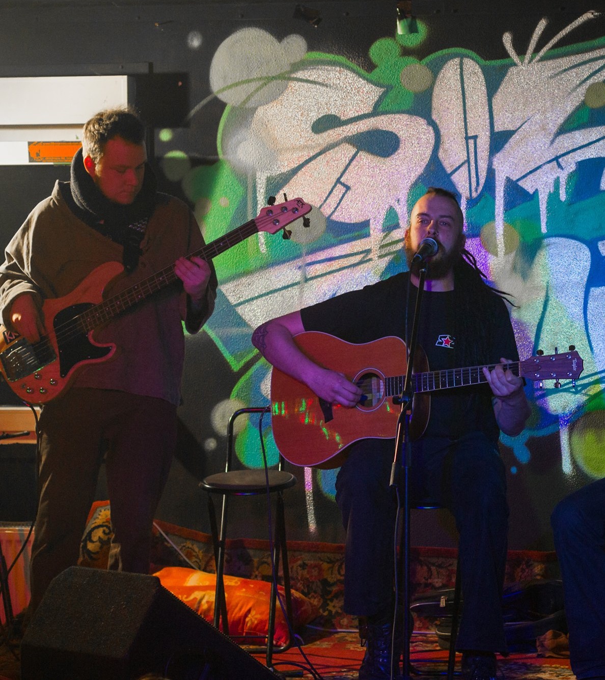 Zwei Personen mit Gitarren vor einer Wand mit Graffiti