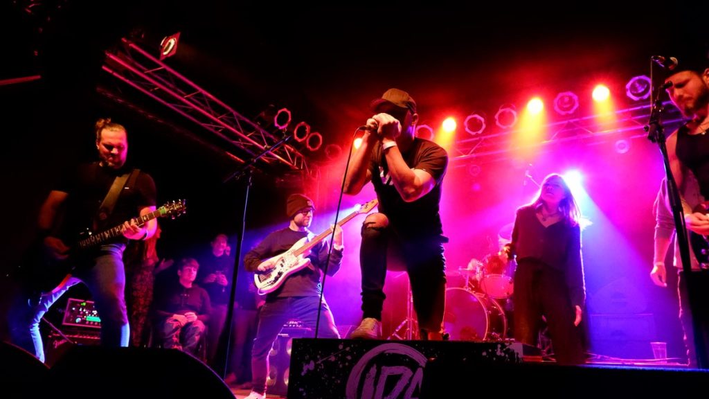 Drei Rockgitarristen, ein Sänger und eine weitere Person performen auf der Bühne